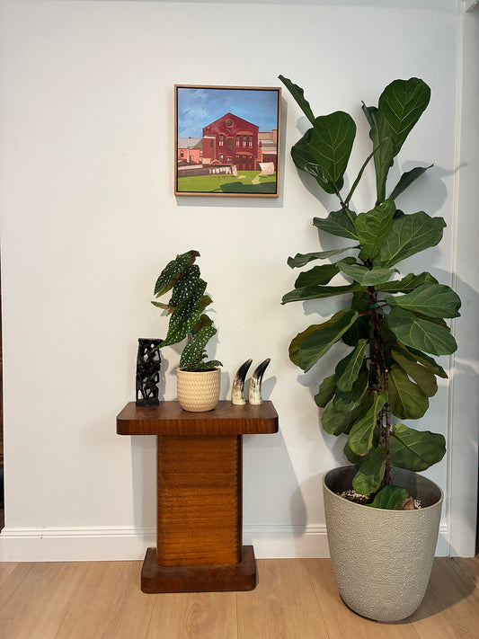 Potted plants on a wooden pedestal against a white wall with a framed picture.
