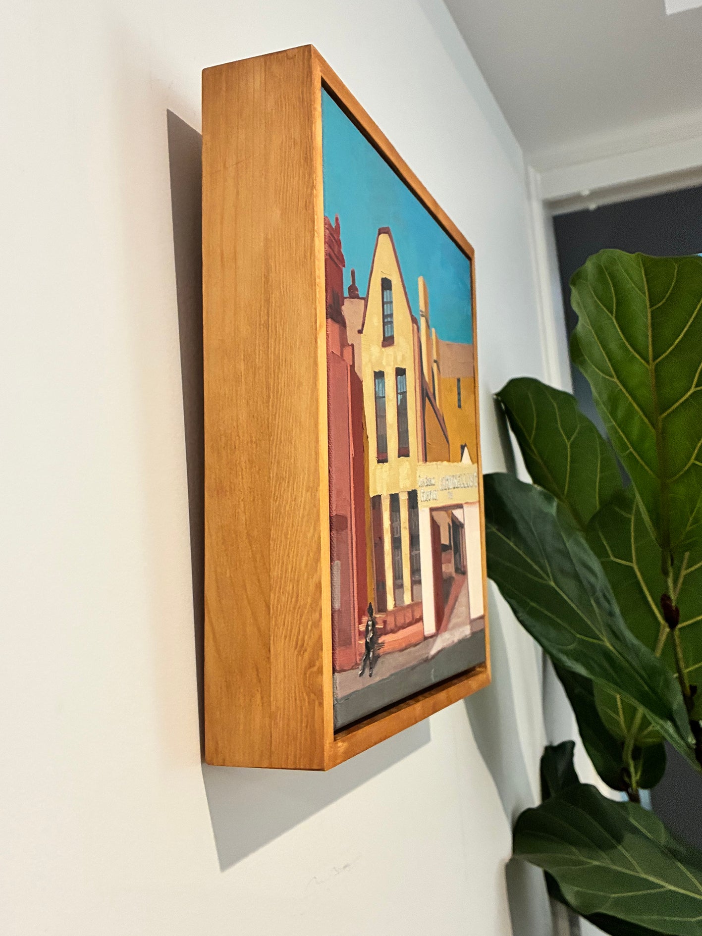Framed artwork on a wall with a plant in the foreground