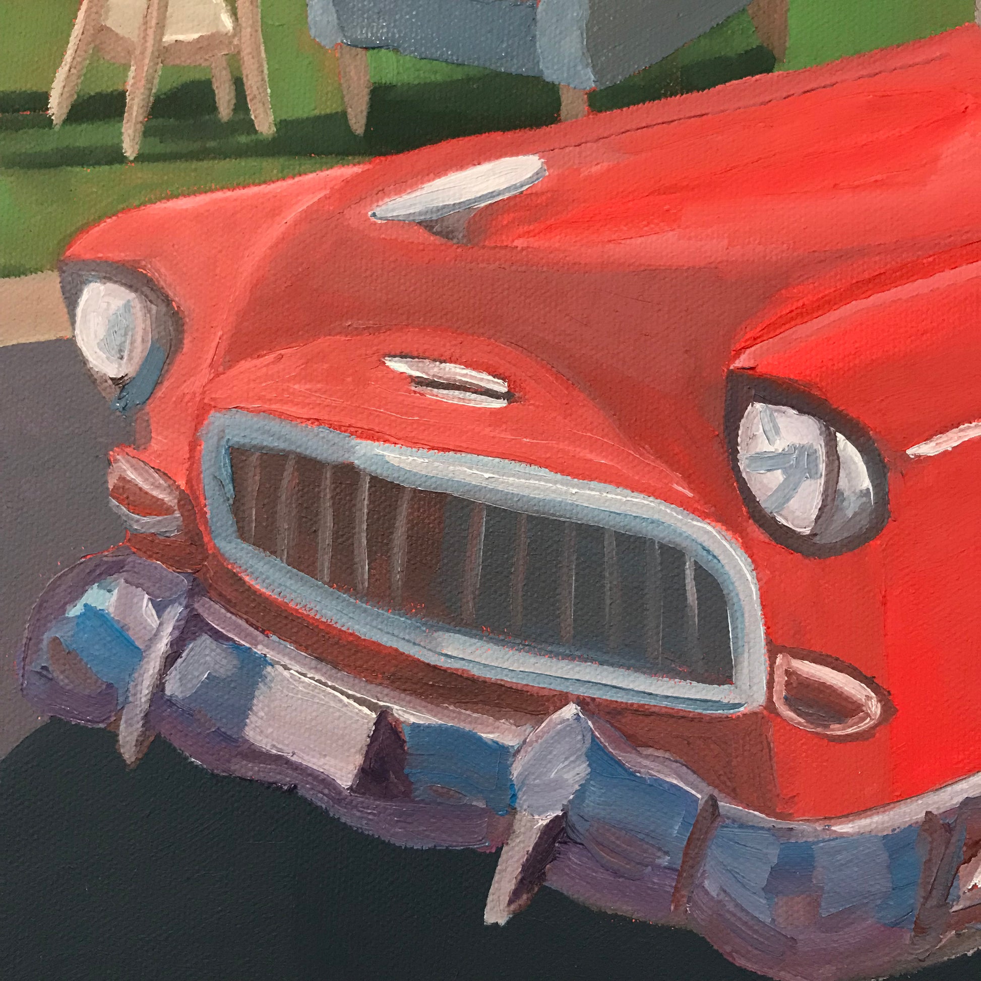 Close-up of a red vintage car's front grille and bumper with blurred background