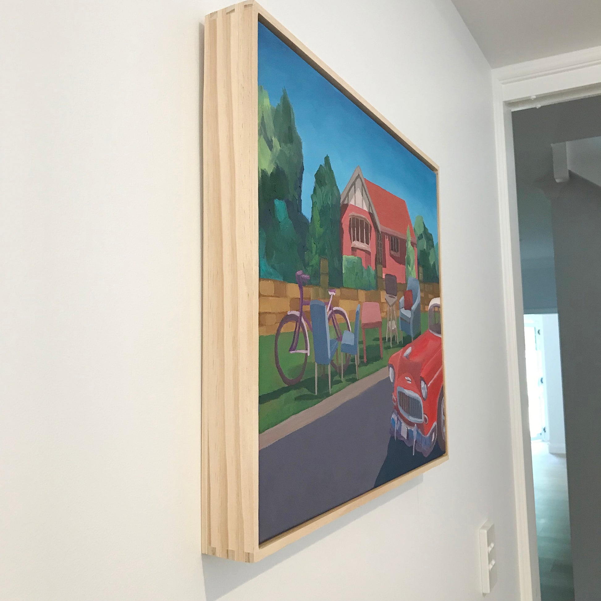 Framed painting of a house with a bicycle and people on a wall.