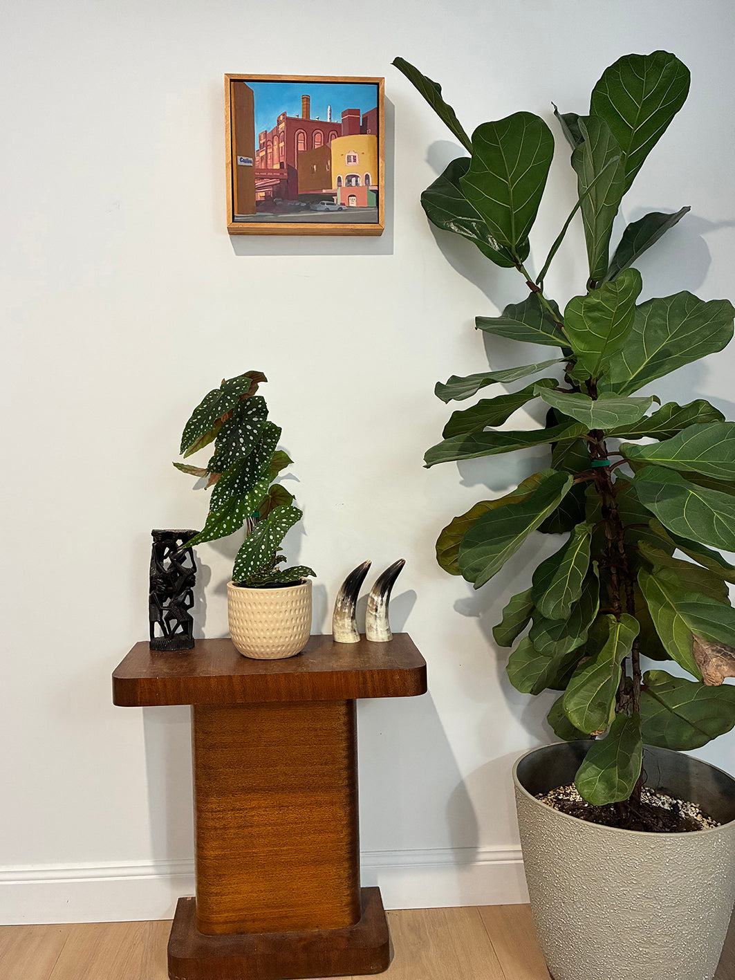Room interior with a wooden side table, potted plants, and a framed picture on the wall.