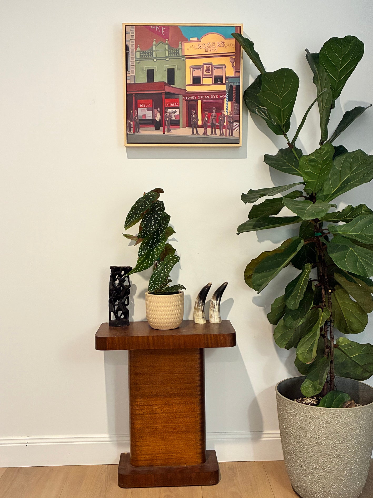 Room interior with a wooden side table, potted plants, and a colorful painting on the wall.