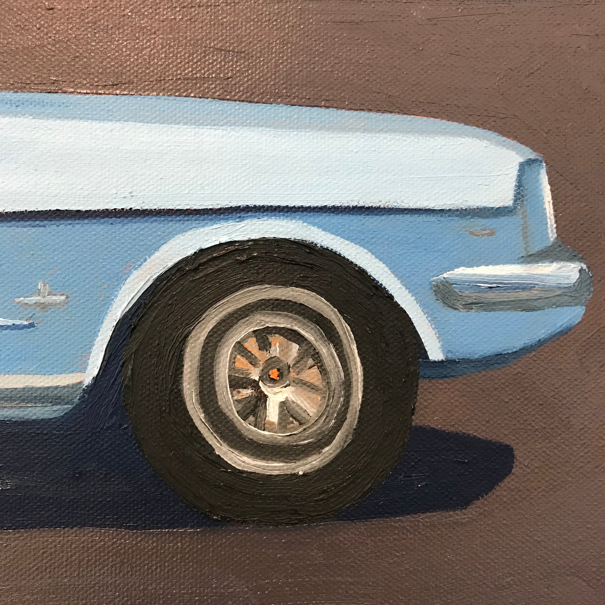 Close-up of a blue car's front wheel on a brown background