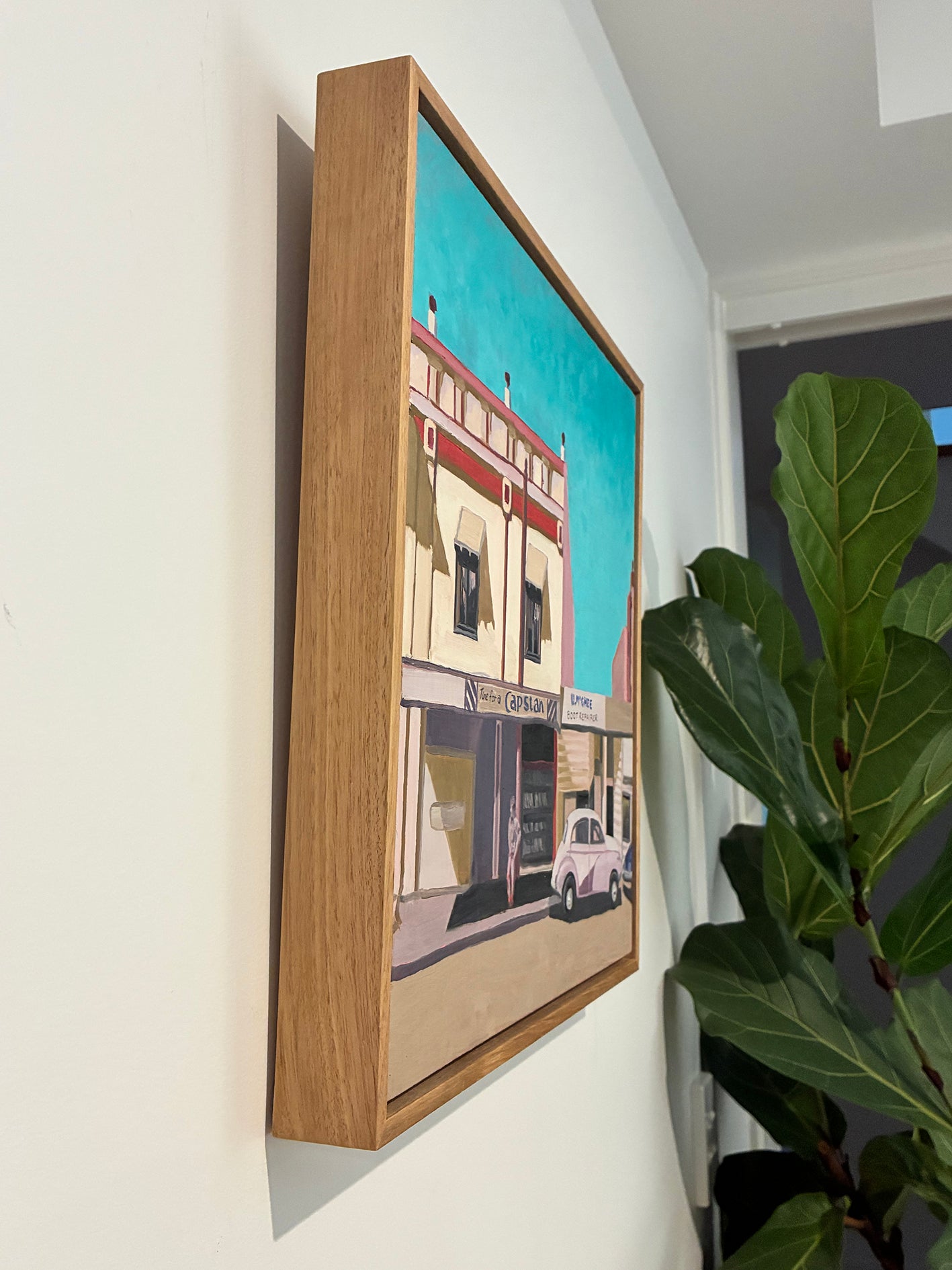 Framed artwork of a building on a wall with a plant in the foreground