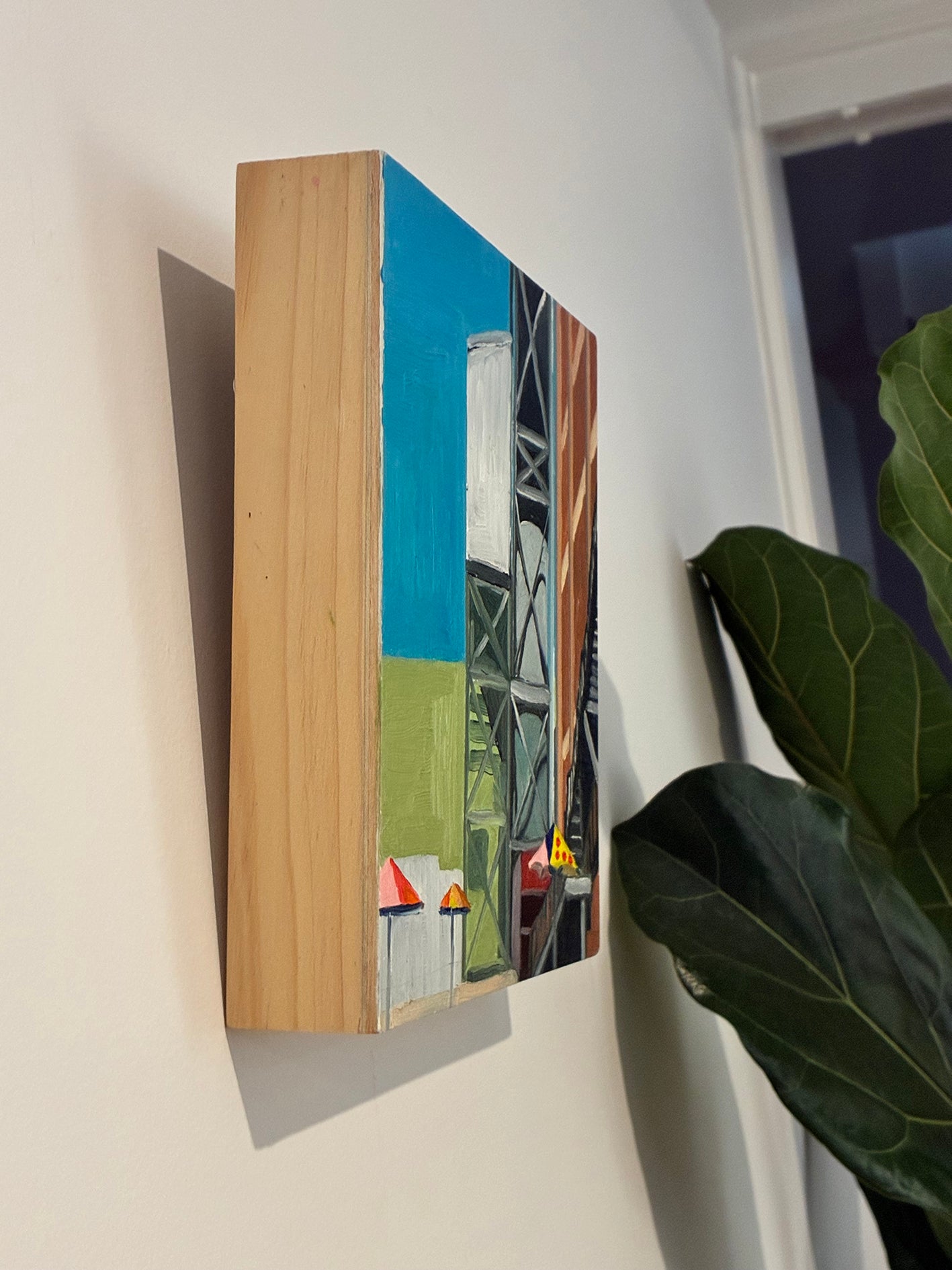 Artistic depiction of a ship on a wooden panel against a white wall with a plant in the corner.