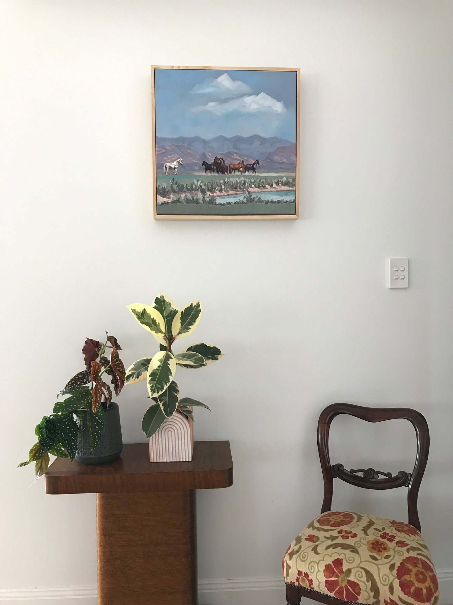 Room interior with a painting on the wall, a chair, and a plant.